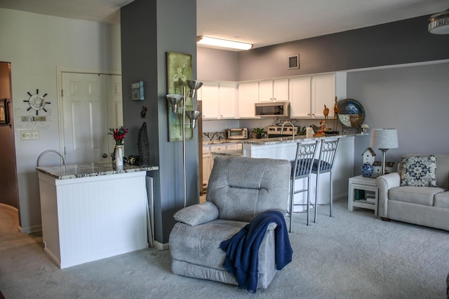 kitchen featuring kitchen peninsula, stone countertops, white cabinetry, and light colored carpet