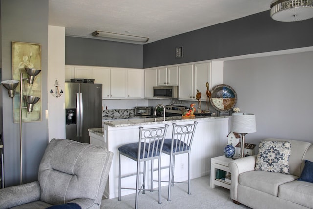 kitchen with sink, light stone counters, light colored carpet, white cabinets, and appliances with stainless steel finishes