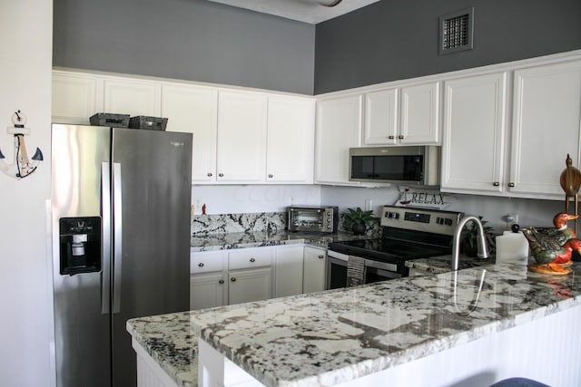 kitchen with kitchen peninsula, appliances with stainless steel finishes, white cabinets, and light stone counters