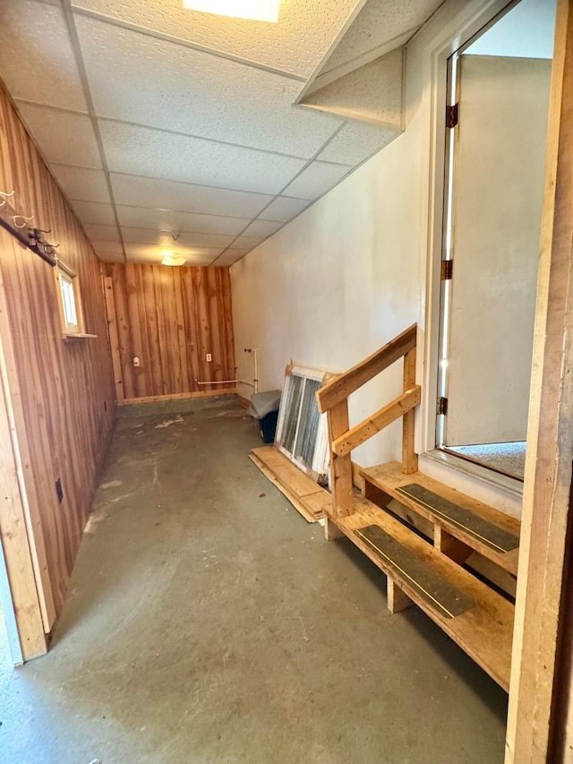 basement with a drop ceiling and wooden walls