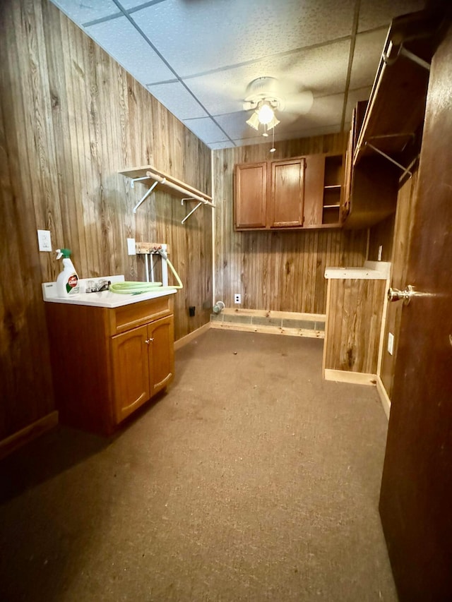 interior space with a drop ceiling, ceiling fan, and wooden walls