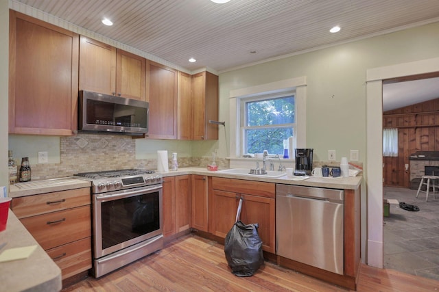 kitchen with sink, stainless steel appliances, light hardwood / wood-style flooring, wooden walls, and ornamental molding