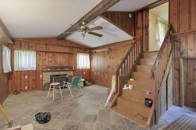 interior space with lofted ceiling with beams, ceiling fan, a fireplace, and wooden walls