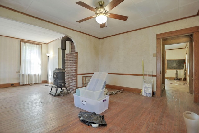 interior space with a wood stove, ceiling fan, ornamental molding, and hardwood / wood-style flooring