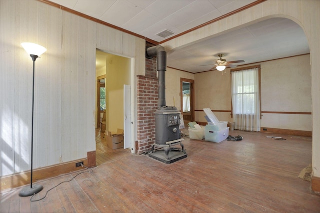 interior space featuring hardwood / wood-style flooring, ceiling fan, a wood stove, and ornamental molding