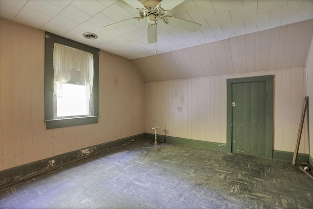 additional living space with dark parquet floors, ceiling fan, lofted ceiling, and wood walls