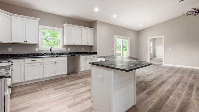 kitchen featuring white cabinets, a center island, light wood-type flooring, and lofted ceiling