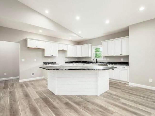 kitchen with white cabinets, a kitchen island, sink, and vaulted ceiling