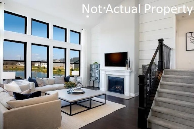 living room featuring a fireplace with flush hearth, recessed lighting, a towering ceiling, wood finished floors, and stairs