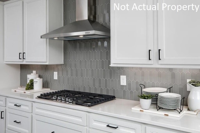 kitchen with wall chimney range hood, white cabinetry, stainless steel gas stovetop, and light countertops