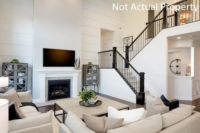 living room with stairway, wood finished floors, a glass covered fireplace, and a towering ceiling