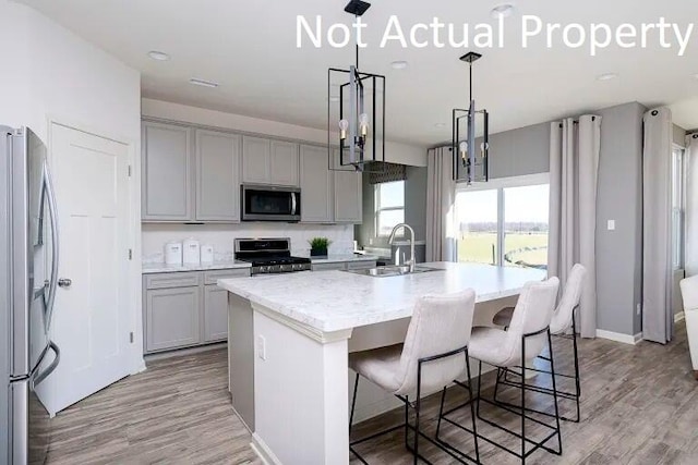 kitchen featuring appliances with stainless steel finishes, sink, hanging light fixtures, light hardwood / wood-style floors, and a center island with sink