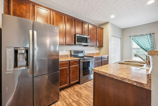 kitchen featuring sink, stainless steel appliances, a textured ceiling, and light hardwood / wood-style floors