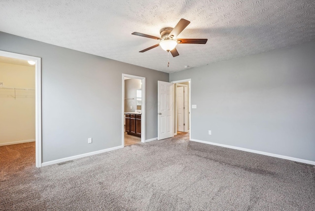 unfurnished bedroom featuring ensuite bathroom, a textured ceiling, ceiling fan, a spacious closet, and a closet