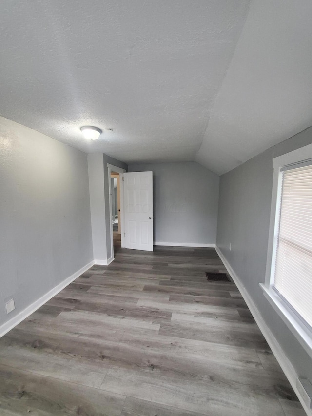 unfurnished room featuring a textured ceiling, lofted ceiling, and dark hardwood / wood-style floors