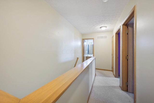 corridor featuring a textured ceiling and light carpet