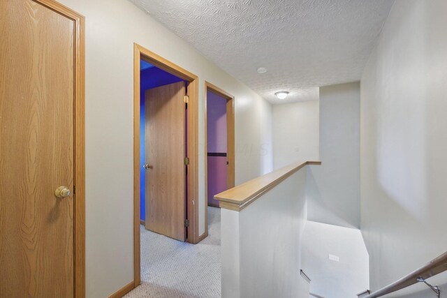 hall featuring a textured ceiling and light colored carpet