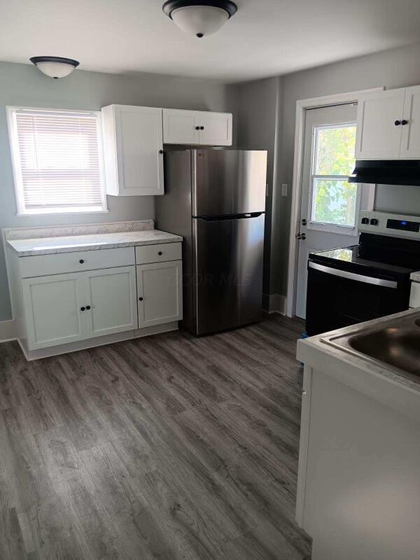 kitchen with white cabinetry, dark hardwood / wood-style flooring, range hood, and appliances with stainless steel finishes