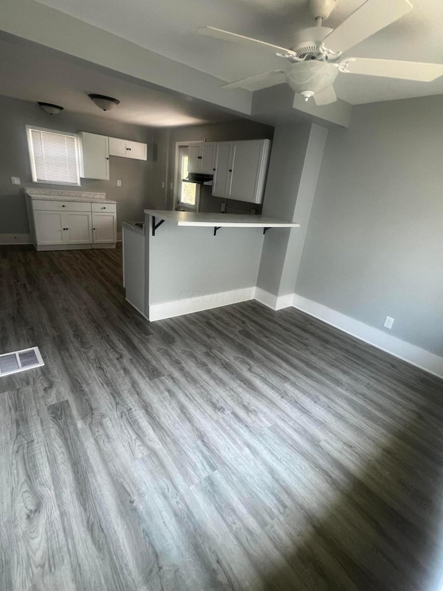 kitchen with kitchen peninsula, a breakfast bar, ceiling fan, white cabinets, and dark hardwood / wood-style floors