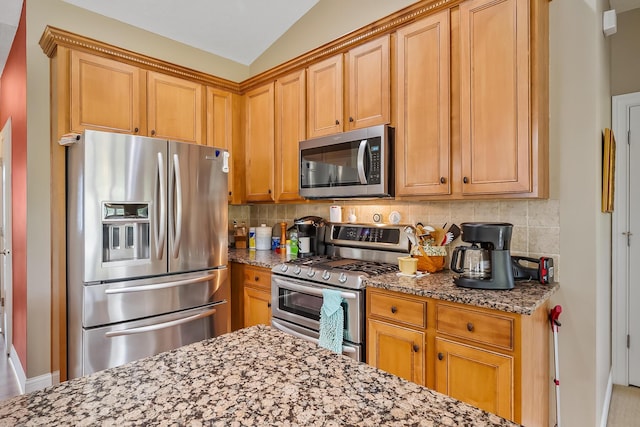 kitchen with tasteful backsplash, light stone countertops, stainless steel appliances, and vaulted ceiling