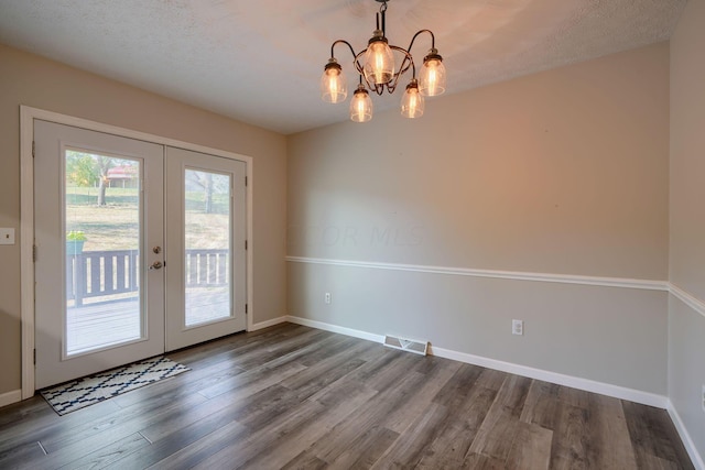 interior space with french doors, a textured ceiling, hardwood / wood-style flooring, and an inviting chandelier