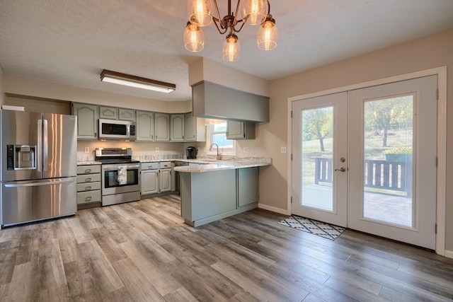 kitchen with kitchen peninsula, appliances with stainless steel finishes, french doors, wood-type flooring, and hanging light fixtures