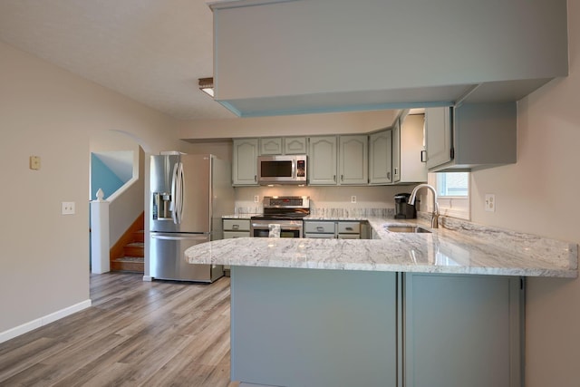 kitchen with kitchen peninsula, stainless steel appliances, sink, wood-type flooring, and gray cabinets