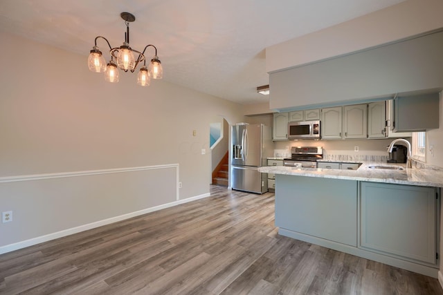 kitchen featuring kitchen peninsula, appliances with stainless steel finishes, sink, hardwood / wood-style flooring, and an inviting chandelier