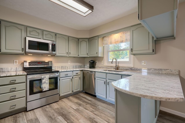 kitchen with sink, kitchen peninsula, a textured ceiling, appliances with stainless steel finishes, and light wood-type flooring