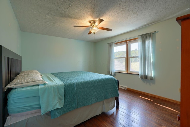 bedroom with a textured ceiling, ceiling fan, and dark wood-type flooring