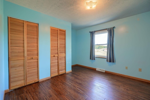 unfurnished bedroom featuring multiple closets, a textured ceiling, and dark wood-type flooring