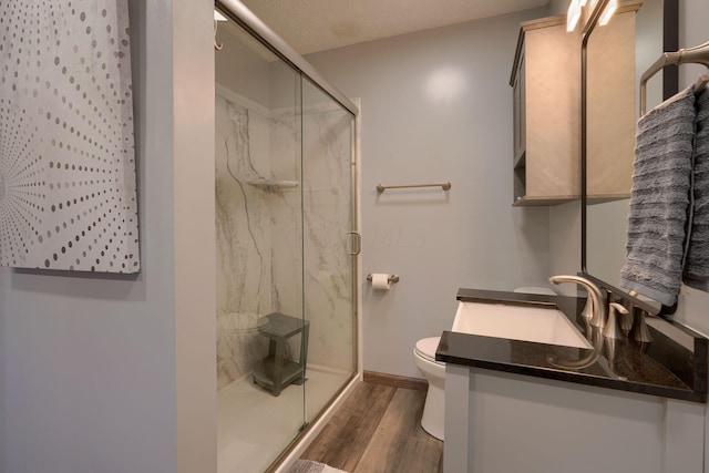 bathroom featuring wood-type flooring, a textured ceiling, toilet, vanity, and a shower with shower door