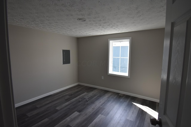 empty room featuring a textured ceiling, electric panel, and dark wood-type flooring