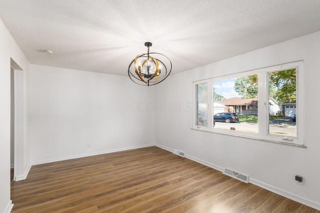 empty room featuring wood-type flooring, a textured ceiling, and a notable chandelier