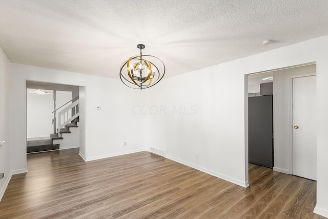 unfurnished room with a textured ceiling, dark wood-type flooring, and an inviting chandelier