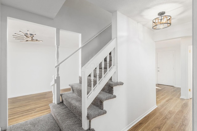 stairway with wood-type flooring, a textured ceiling, and an inviting chandelier