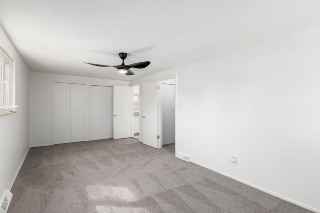 unfurnished bedroom featuring multiple closets, ceiling fan, and light carpet