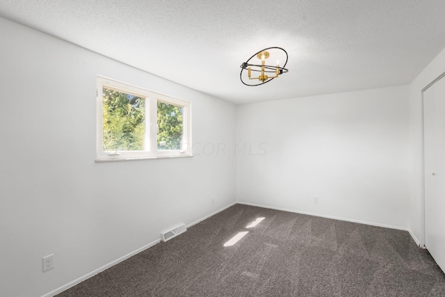 empty room with dark colored carpet and a textured ceiling