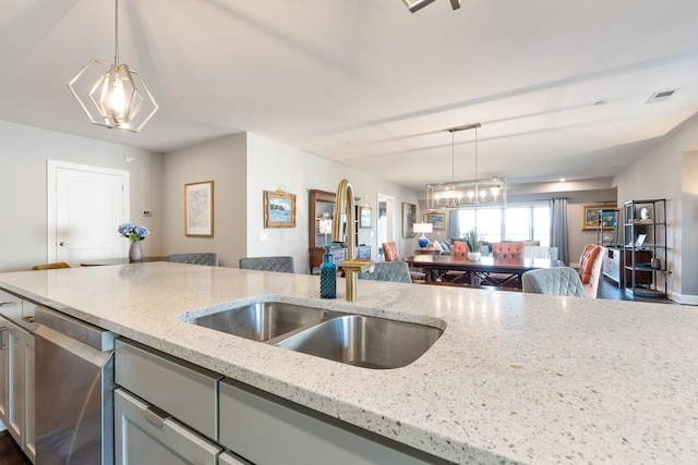 kitchen featuring light stone countertops, decorative light fixtures, stainless steel dishwasher, and sink