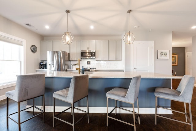 kitchen featuring pendant lighting, dark hardwood / wood-style flooring, stainless steel appliances, and an island with sink