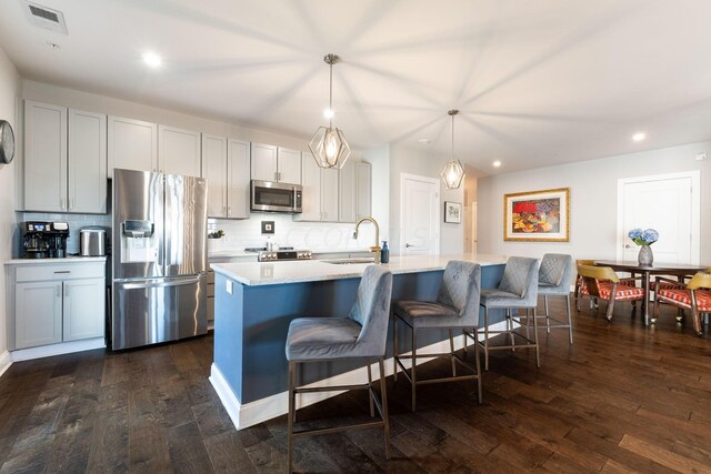 kitchen featuring dark hardwood / wood-style flooring, stainless steel appliances, sink, pendant lighting, and a center island with sink