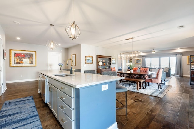 kitchen with dark wood-type flooring, a kitchen island with sink, sink, and hanging light fixtures