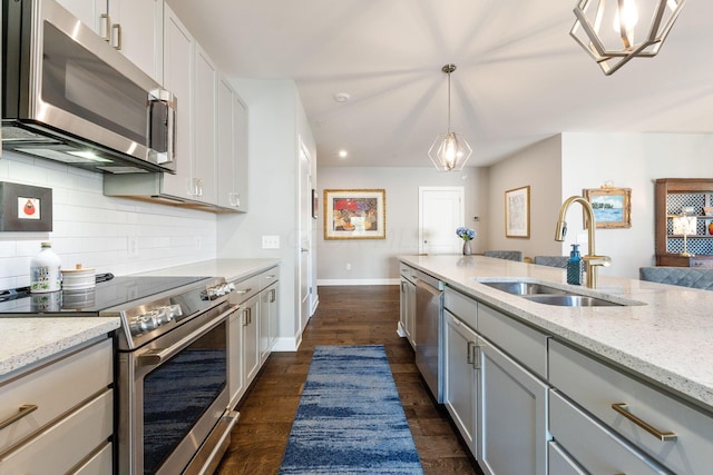 kitchen with light stone countertops, stainless steel appliances, sink, pendant lighting, and dark hardwood / wood-style floors