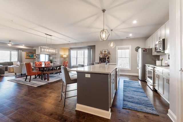 kitchen with pendant lighting, dark wood-type flooring, white cabinets, a kitchen breakfast bar, and an island with sink