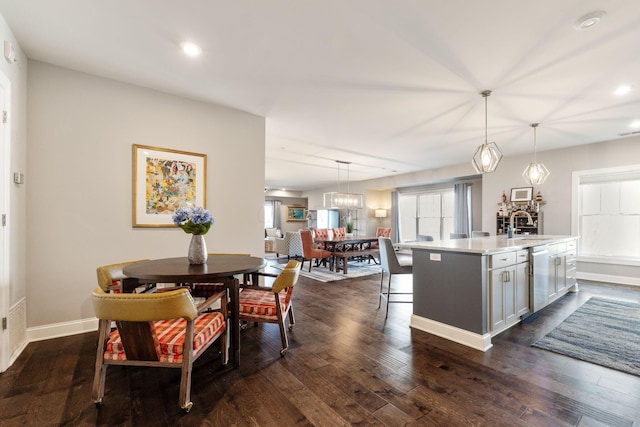 kitchen with sink, dark wood-type flooring, stainless steel dishwasher, decorative light fixtures, and a kitchen island with sink