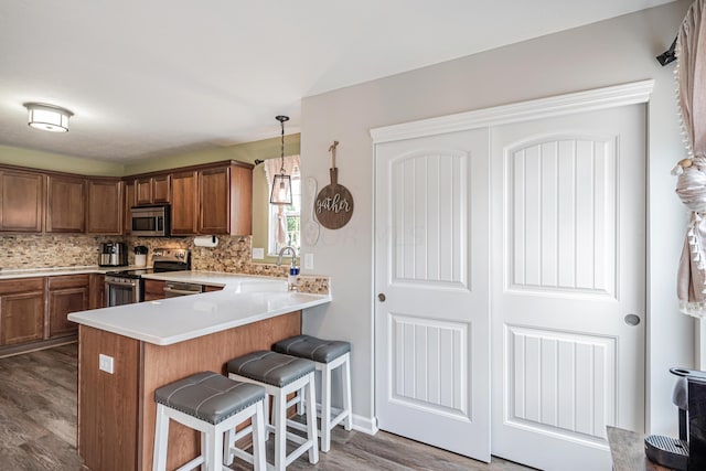 kitchen featuring sink, hanging light fixtures, dark hardwood / wood-style flooring, kitchen peninsula, and stainless steel appliances