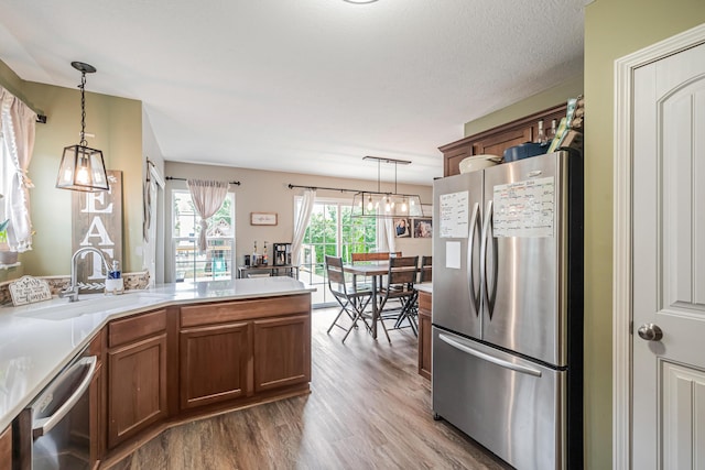 kitchen with pendant lighting, sink, a textured ceiling, light hardwood / wood-style floors, and stainless steel appliances