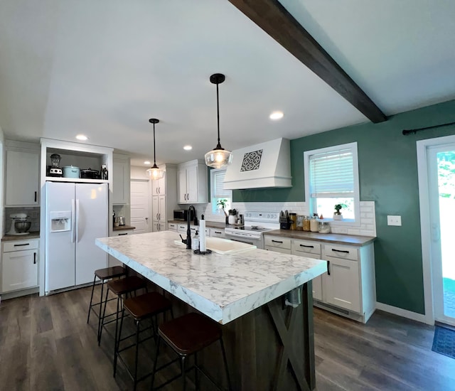 kitchen with custom range hood, white appliances, decorative light fixtures, and plenty of natural light