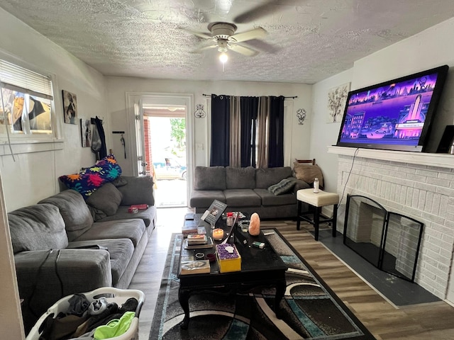 living room with hardwood / wood-style floors, a textured ceiling, a brick fireplace, and ceiling fan