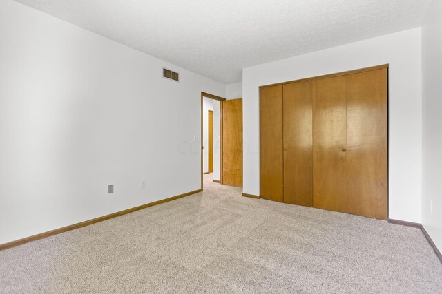 unfurnished bedroom with light carpet, a closet, and a textured ceiling